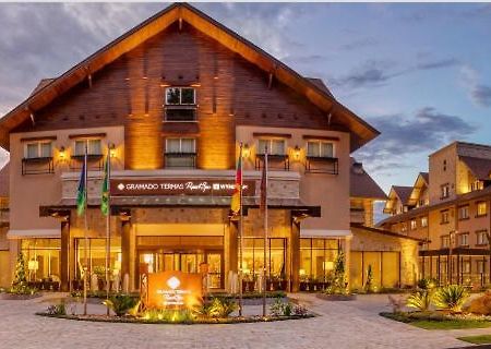 Wyndham Gramado Termas Resort & Spa Exterior foto The photo shows a charming lodge or hotel building with a wooden exterior, characterized by a sloping roof and multiple windows. The entrance is well-lit and features a sign that appears to identify the establishment. There are several flags displaye