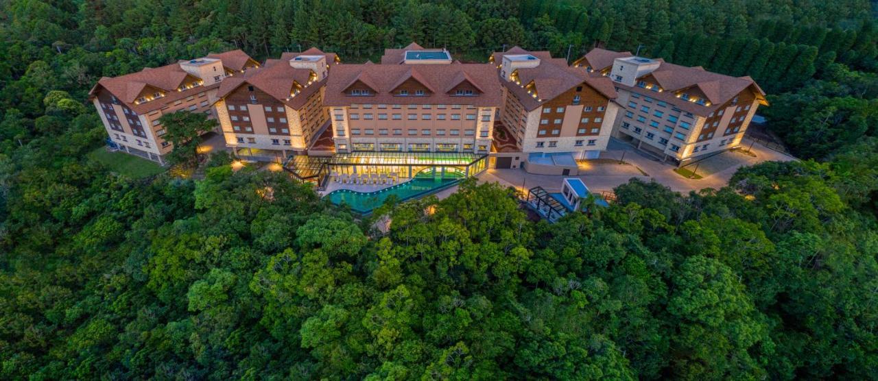Wyndham Gramado Termas Resort & Spa Exterior foto The photo shows a resort or hotel complex surrounded by lush greenery. The buildings have a modern design with multiple stories, featuring a mix of large windows and distinctive roofs. There is a swimming pool area visible, which appears to be integr