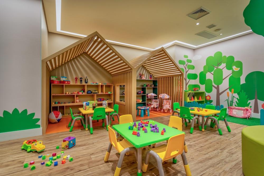 Wyndham Gramado Termas Resort & Spa Exterior foto The photo shows a colorful and playful children's playroom. There are two wooden playhouses with slatted roofs, which create a cozy atmosphere. Surrounding the playhouses are vibrant green wall decorations depicting trees and nature. 

In the center 