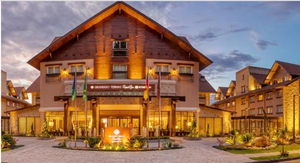 Wyndham Gramado Termas Resort & Spa Exterior foto The photo shows a charming lodge or hotel building with a wooden exterior, characterized by a sloping roof and multiple windows. The entrance is well-lit and features a sign that appears to identify the establishment. There are several flags displaye