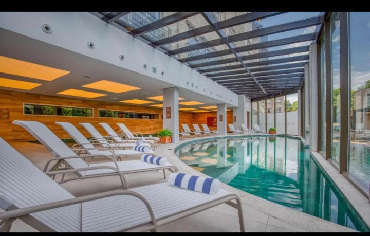Wyndham Gramado Termas Resort & Spa Exterior foto The photo shows an indoor swimming pool area. There are several white lounge chairs positioned around the pool, with some featuring blue and white striped towels. The pool itself is curved and has clear water. The area is well-lit by natural light co