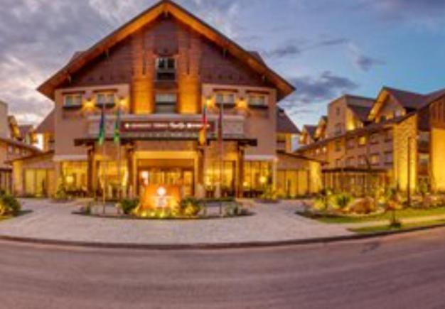 Wyndham Gramado Termas Resort & Spa Exterior foto The photo shows an exterior view of a lodge or hotel, designed in a rustic style with wooden accents. The building features a gable roof, large windows, and well-lit entrance, suggesting a warm and welcoming atmosphere. The landscape around it includ