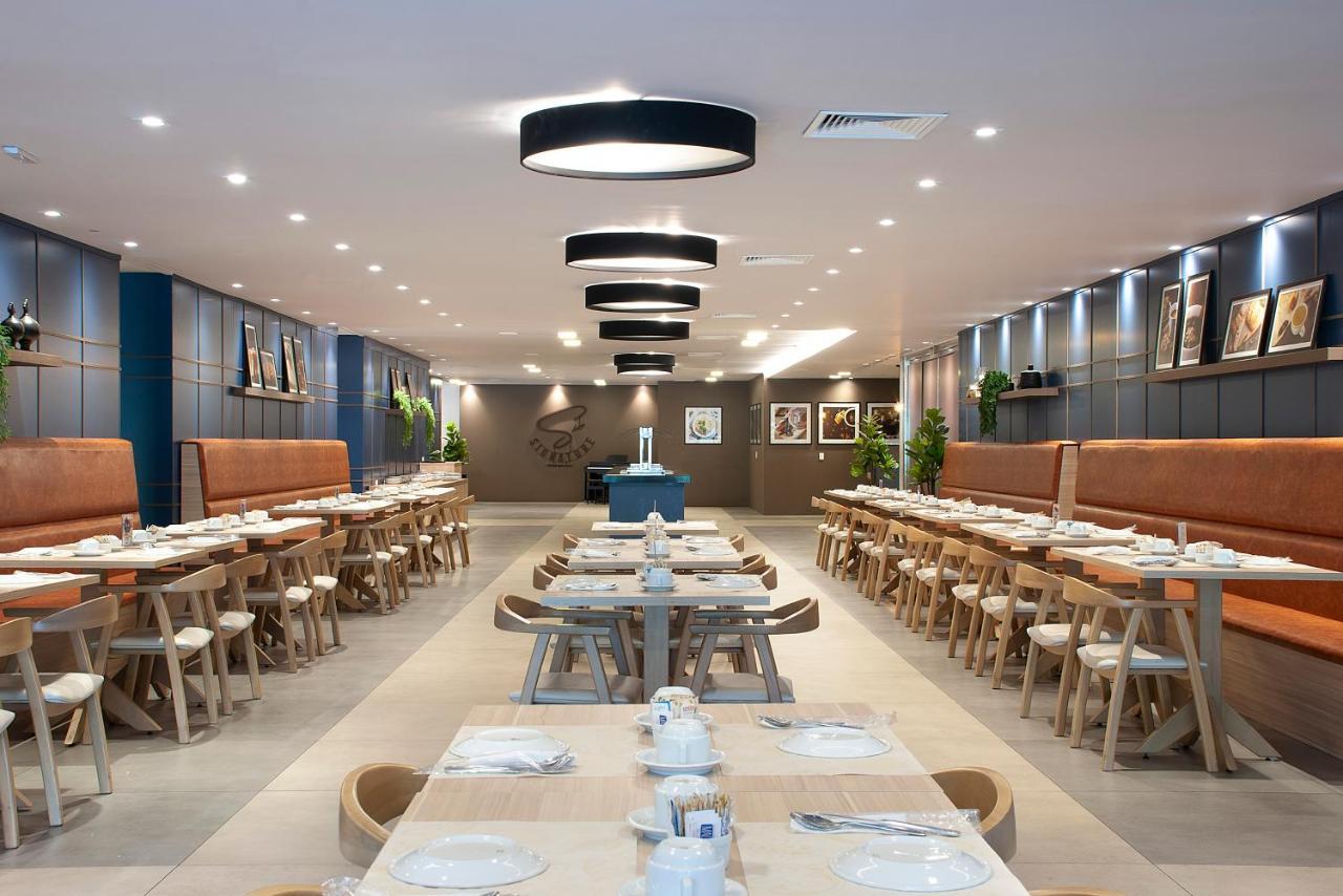 Wyndham Gramado Termas Resort & Spa Exterior foto The photo depicts a modern restaurant interior. The space features long tables arranged with neatly set place settings, including plates and teacups. The decor includes wooden chairs and booths along the walls, creating a clean and inviting atmospher