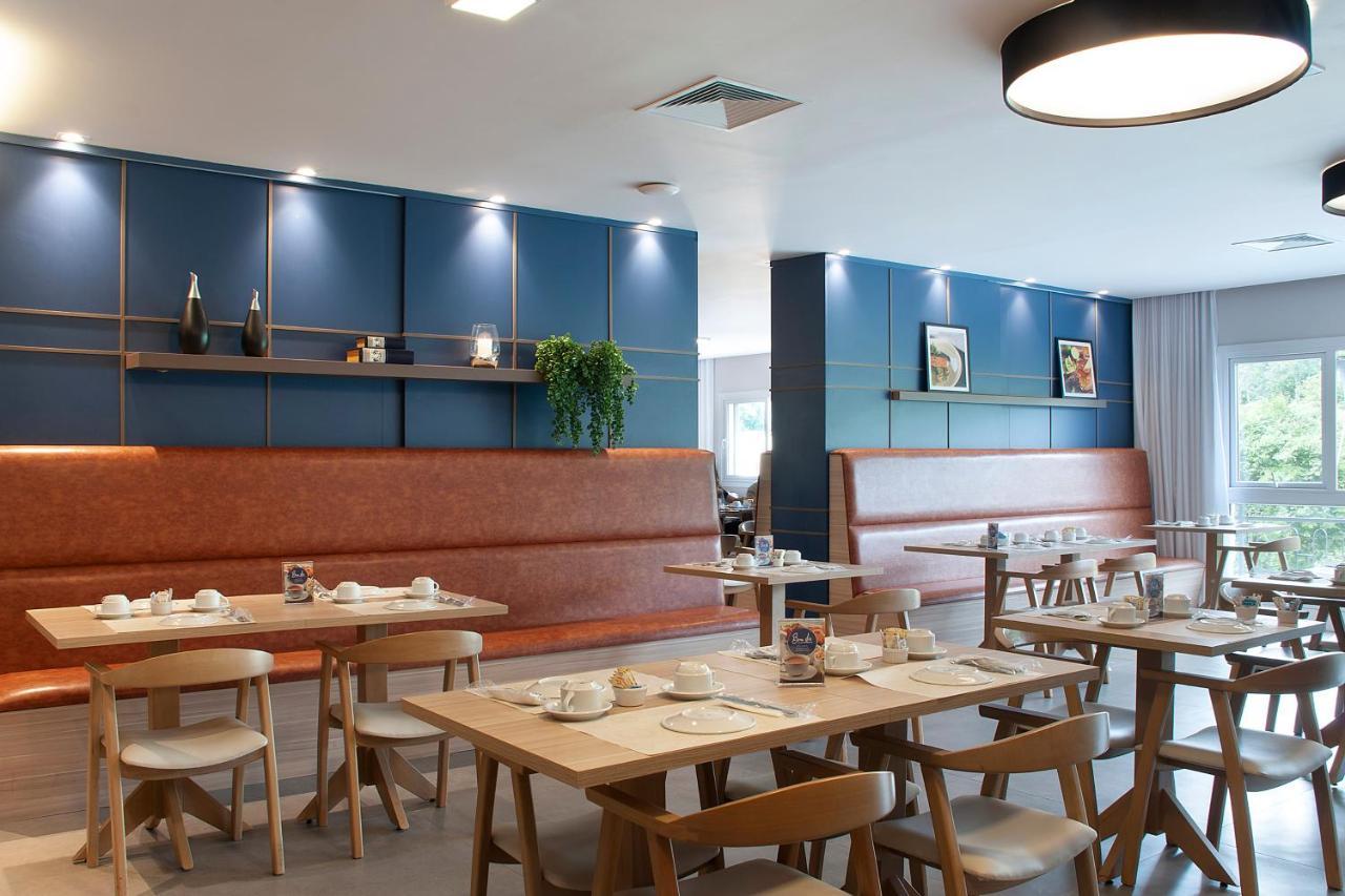 Wyndham Gramado Termas Resort & Spa Exterior foto The photo shows a modern restaurant interior. There are wooden tables arranged with chairs, and the tables have dishes neatly placed on them. The walls are painted a calming blue, with decorative shelves featuring a few items and framed pictures. The
