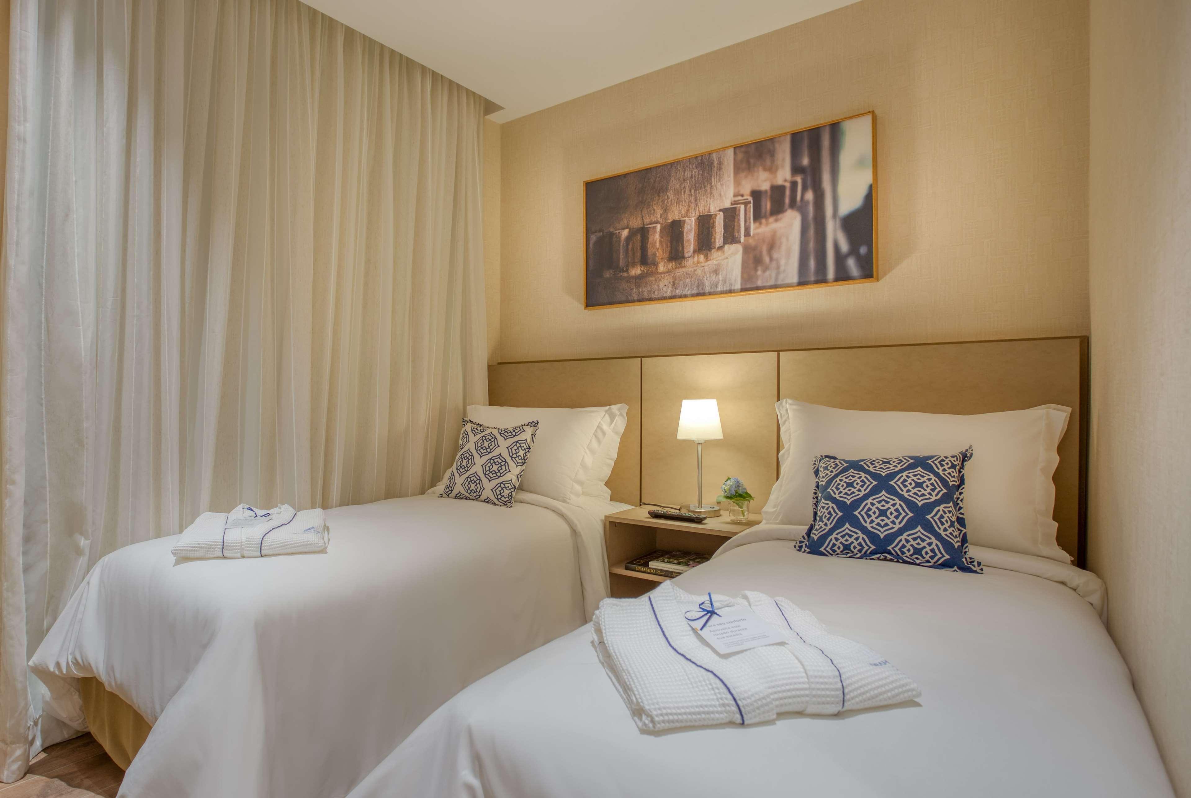 Wyndham Gramado Termas Resort & Spa Exterior foto The photo shows a cozy bedroom featuring two twin beds with light-colored bedding. Each bed has a decorative pillow, and there are neatly folded towels at the foot of the beds. A bedside table is situated between the beds, topped with a small lamp an