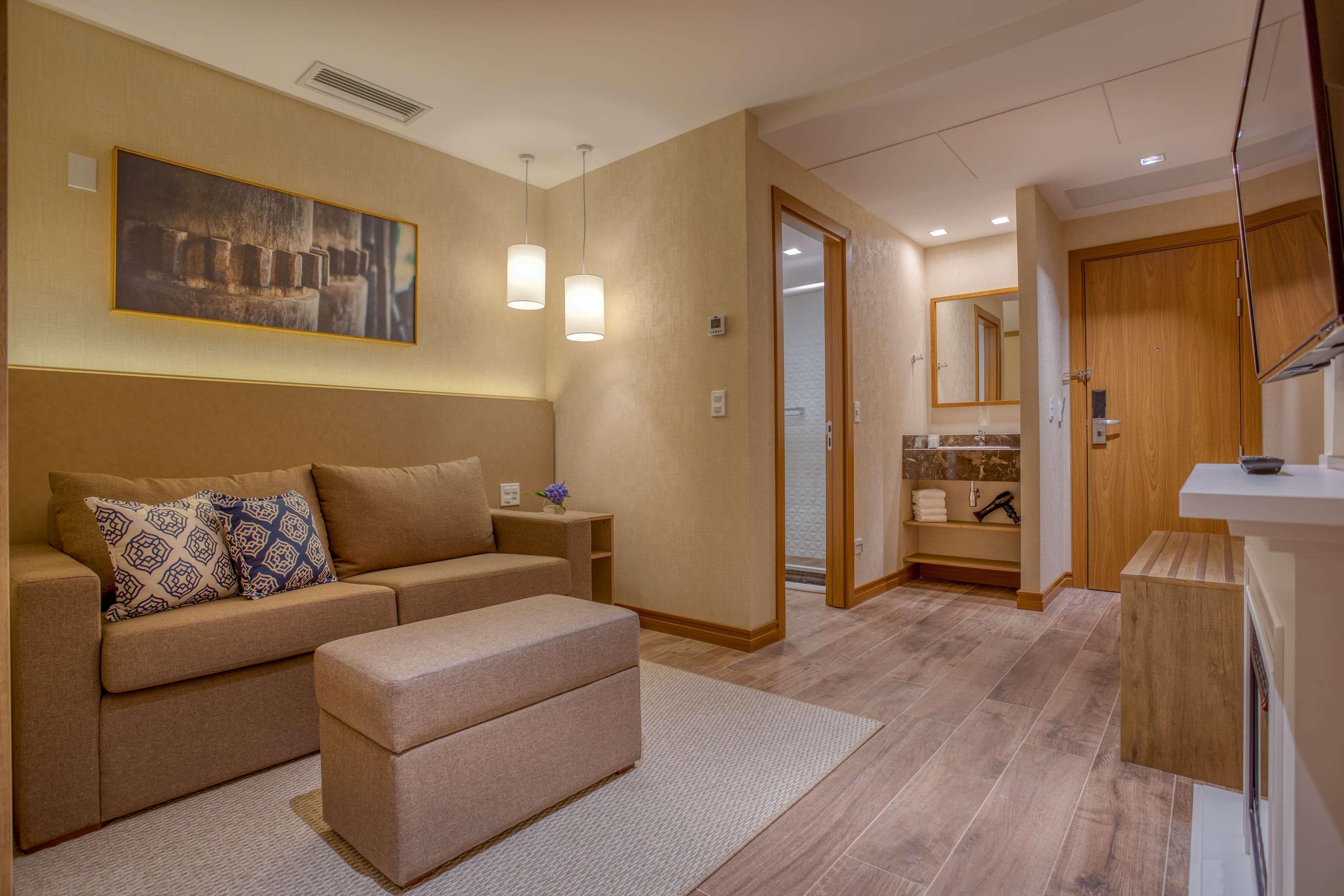 Wyndham Gramado Termas Resort & Spa Exterior foto The photo shows a cozy living space with a modern and inviting design. There is a comfortable sofa with decorative cushions, a small ottoman in front of it, and a light-colored rug on the floor. The walls are painted in soft, warm tones, and two pend