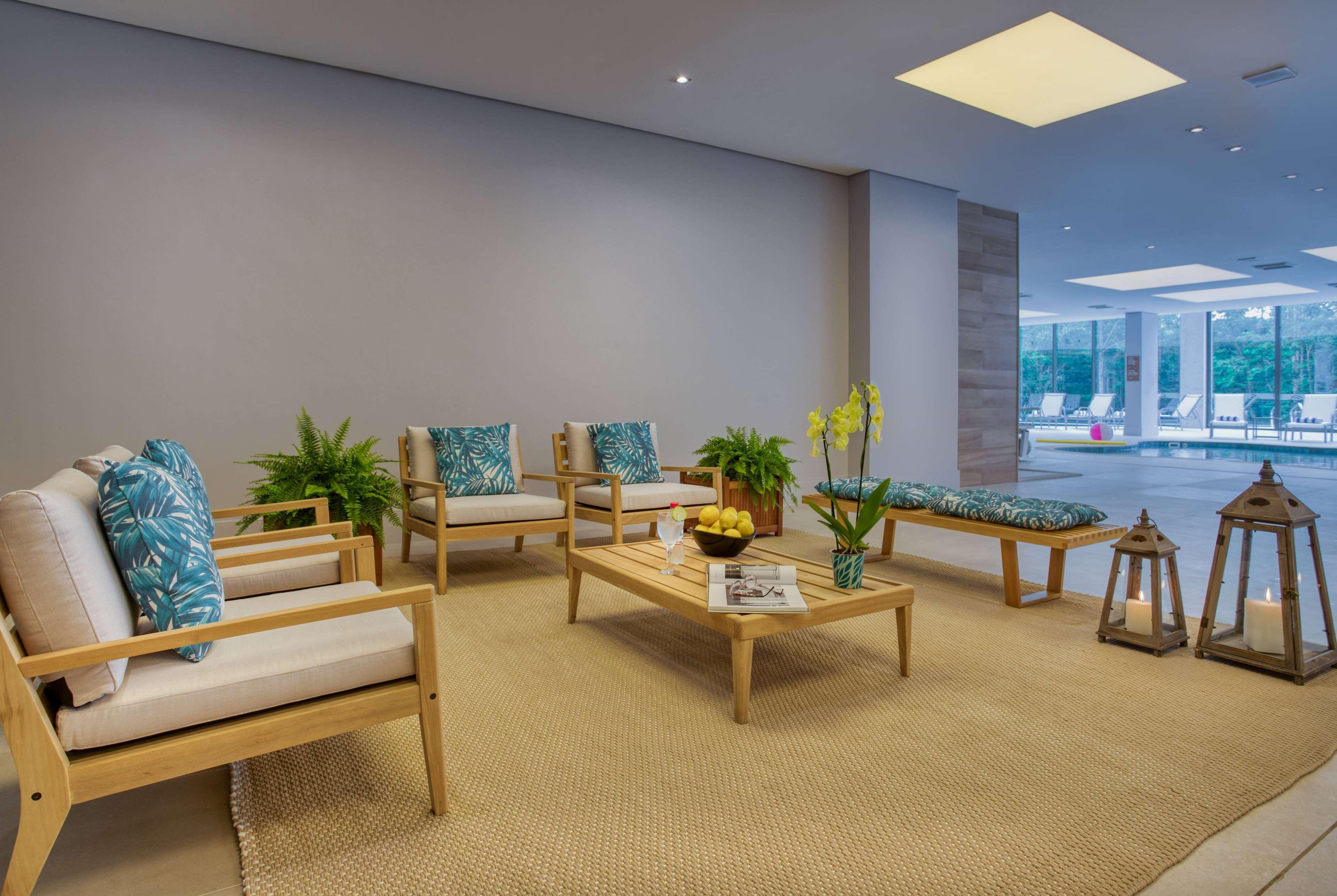Wyndham Gramado Termas Resort & Spa Exterior foto The photo shows a modern and inviting interior space, likely a lounge or waiting area. There are several wooden chairs with light-colored cushions featuring tropical patterns. A low wooden coffee table is centrally placed, adorned with a magazine and
