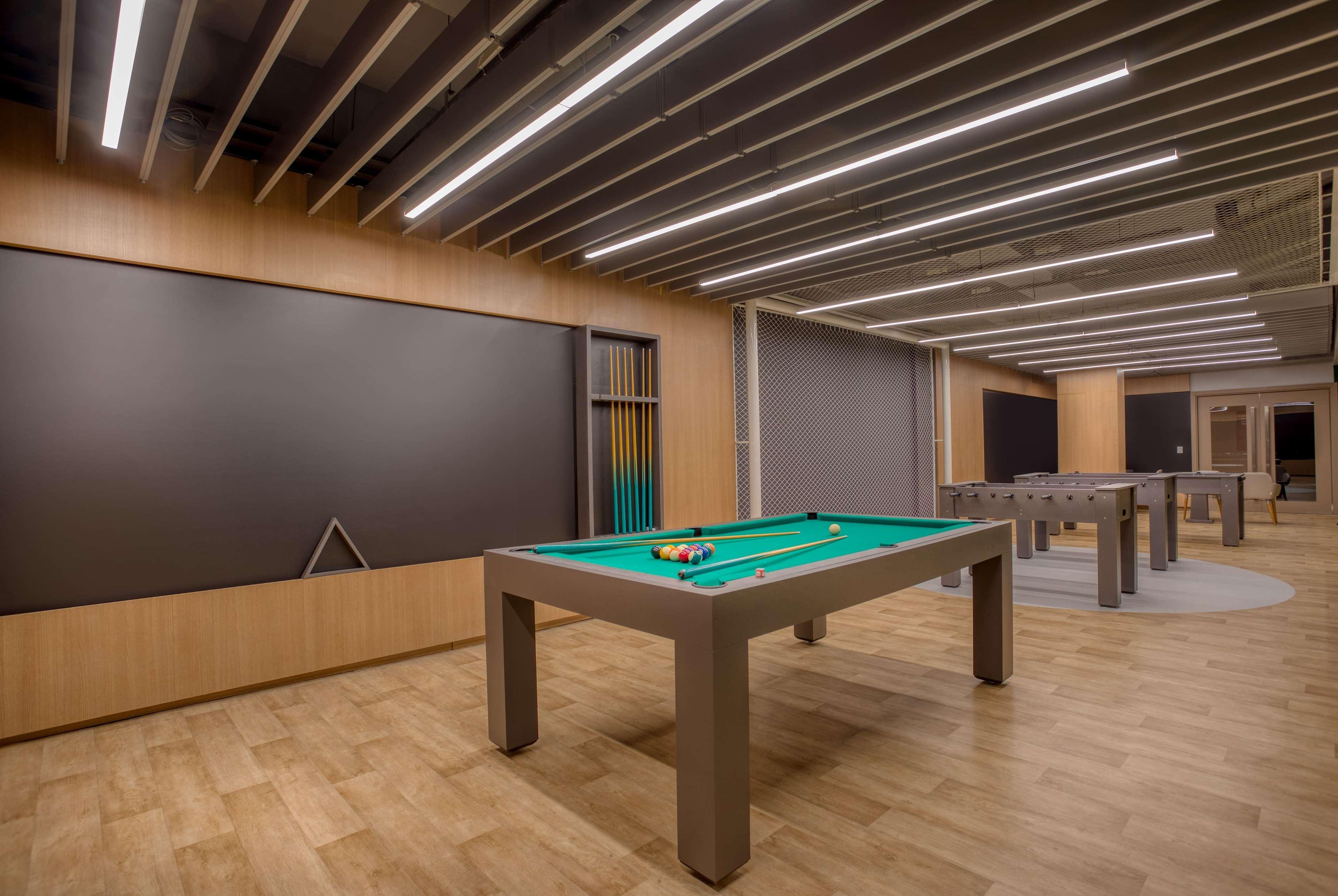 Wyndham Gramado Termas Resort & Spa Exterior foto The photo shows a modern recreational room featuring several pool tables. In the center, there is a green felt pool table with balls arranged on it. The room has wooden flooring and is illuminated by overhead lights with a sleek design. The walls are