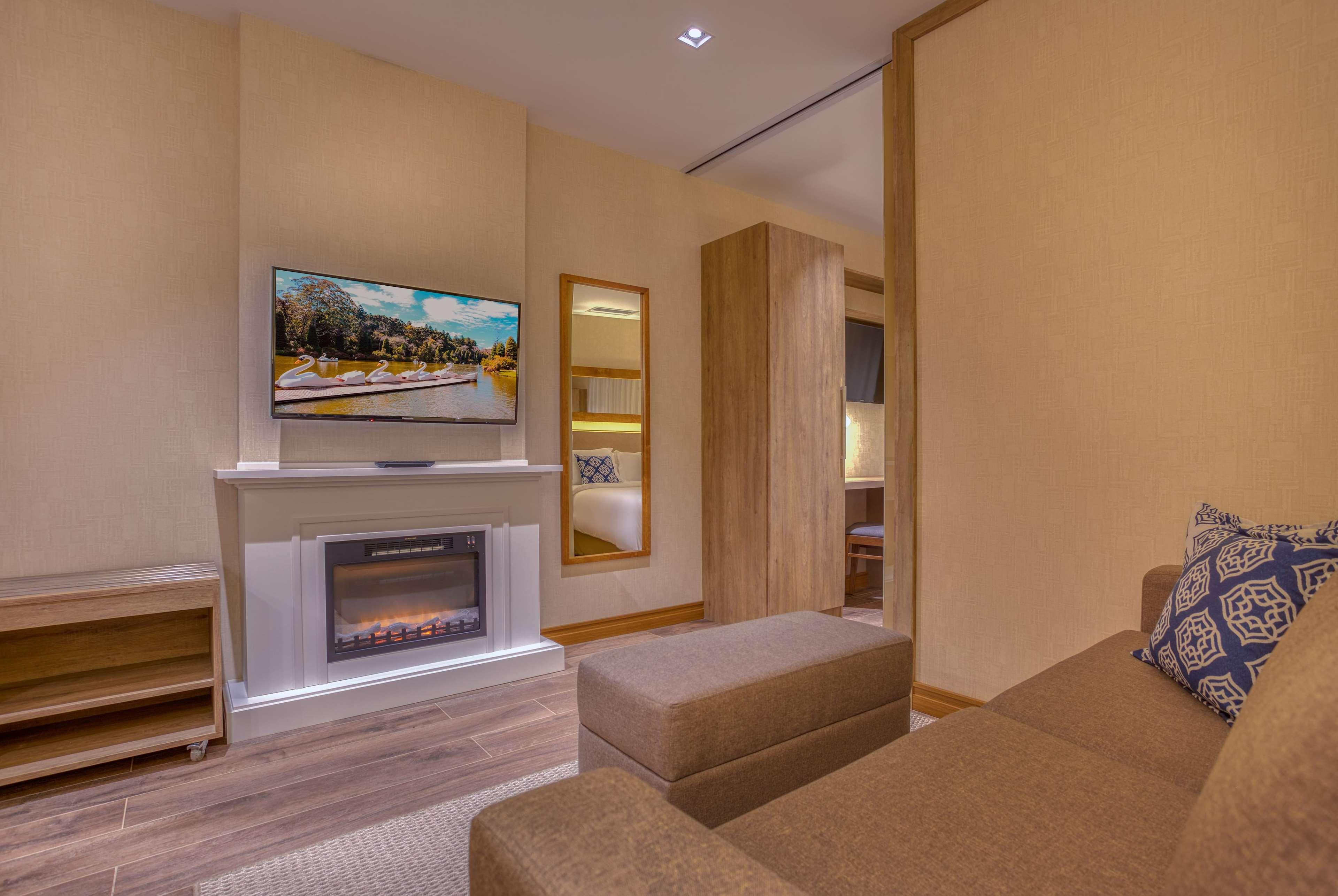 Wyndham Gramado Termas Resort & Spa Exterior foto The photo shows a cozy living space featuring a comfortable sofa, a modern television mounted on the wall, and a stylish electric fireplace beneath it. There is a decorative element on the wall, possibly a small shelf or cabinet. The room is well-lit