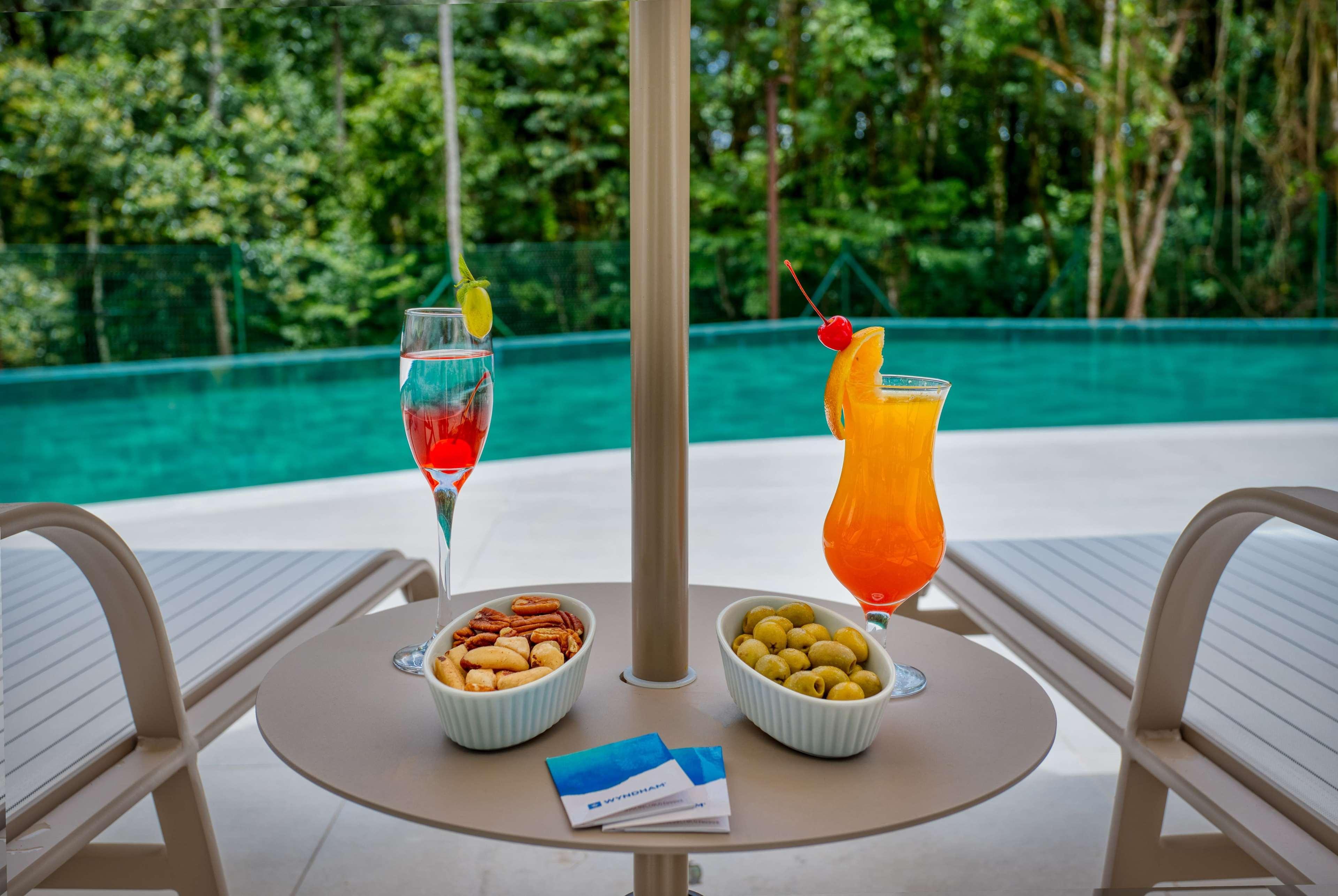 Wyndham Gramado Termas Resort & Spa Exterior foto The photo shows a table on a patio or by a poolside with two vibrant cocktails. One is a pink drink with a lemon slice, and the other is an orange drink garnished with a cherry and an orange slice. There are also two small bowls: one containing mixed