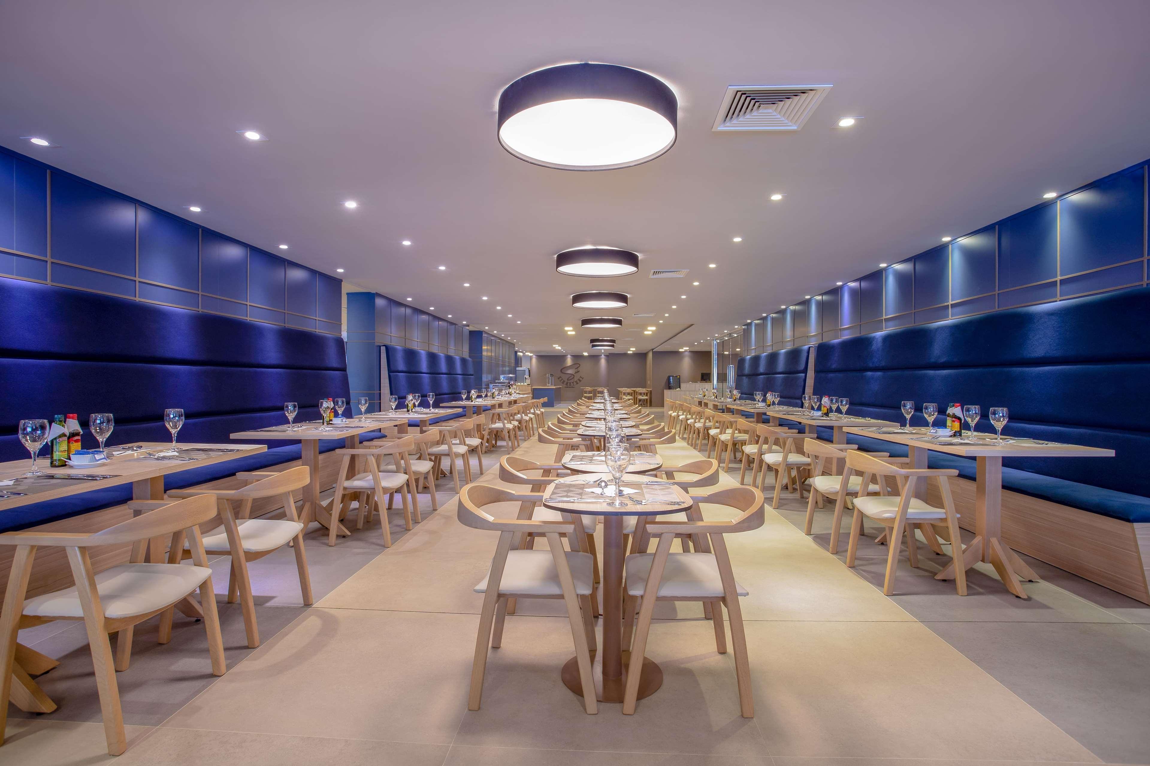Wyndham Gramado Termas Resort & Spa Exterior foto The photo shows a modern dining room with a sleek and contemporary design. There are long rows of wooden tables arranged with chairs, indicating it can accommodate a number of guests. The walls are a deep blue color, complemented by bright overhead l