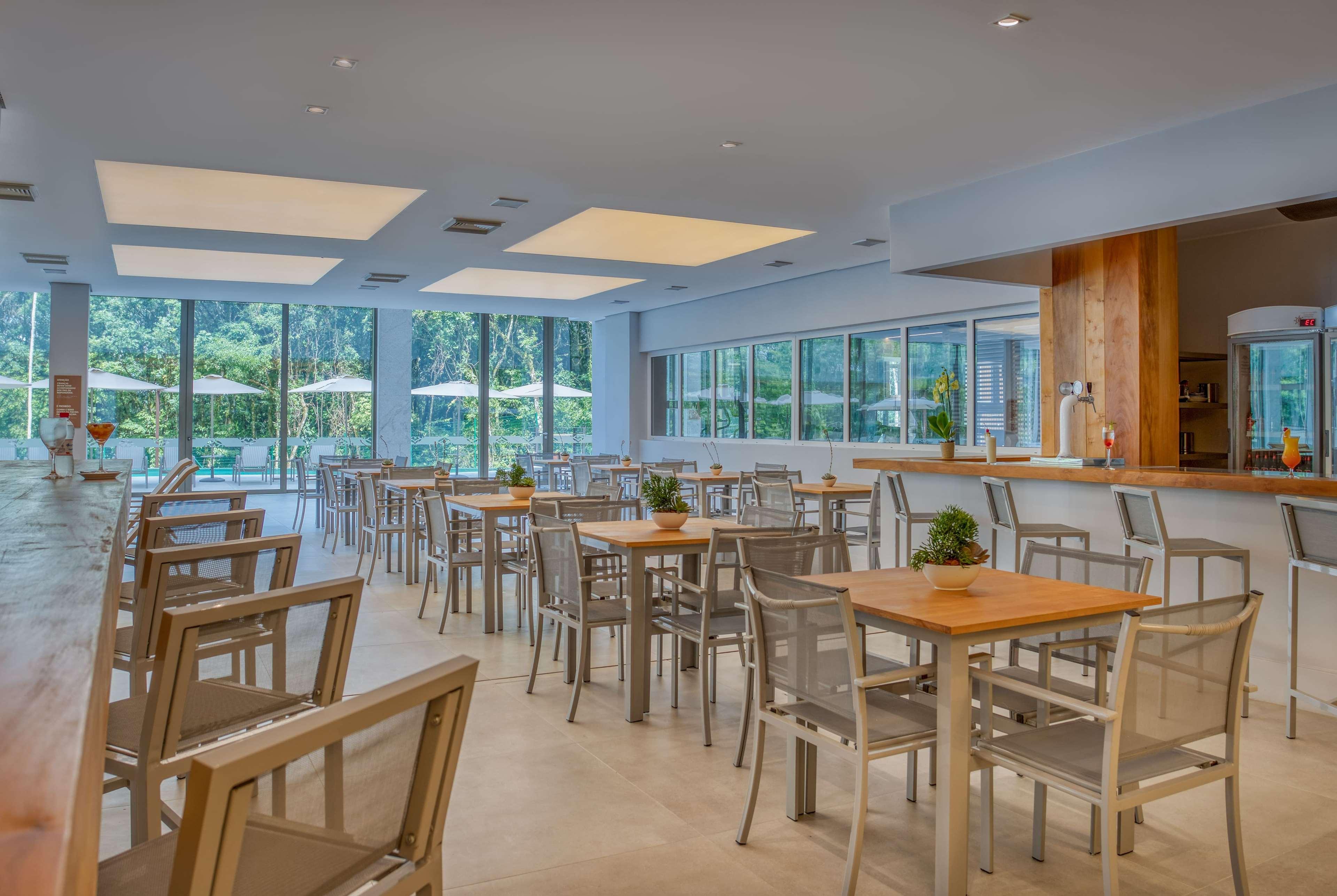 Wyndham Gramado Termas Resort & Spa Exterior foto The image shows a dining area or restaurant with a modern and spacious design. There are several tables with chairs arranged neatly throughout the space. The walls are light-colored, and large windows allow plenty of natural light to fill the room, o