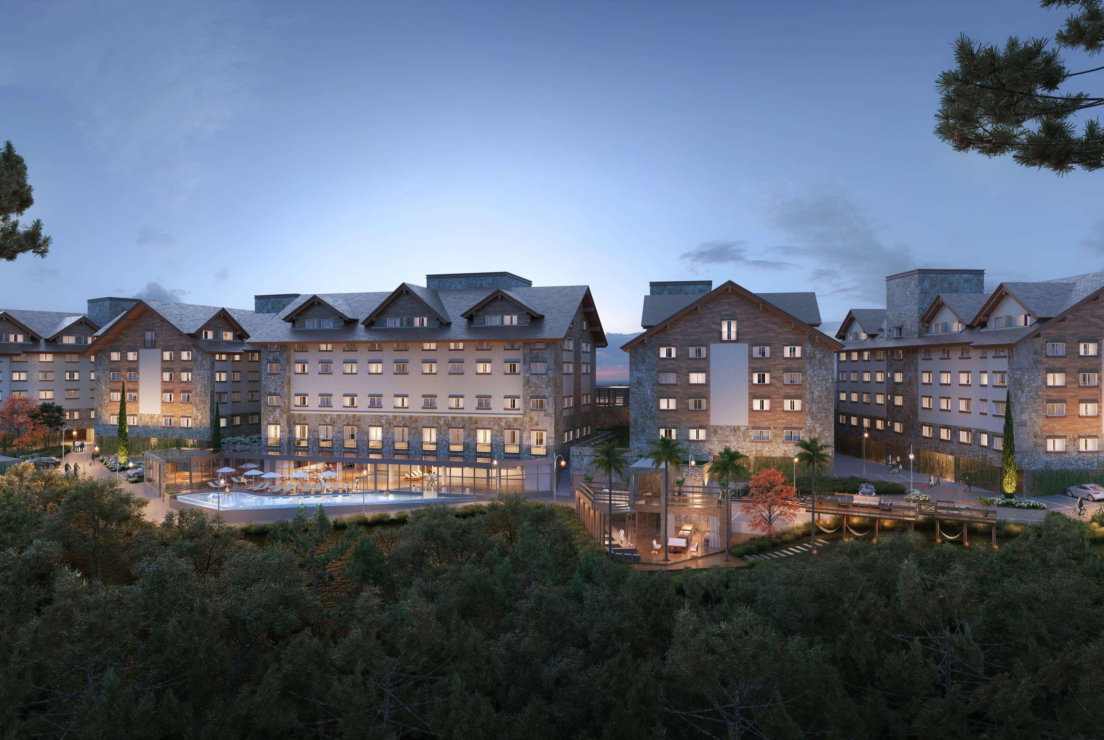 Wyndham Gramado Termas Resort & Spa Exterior foto The photo depicts a modern hotel complex nestled in a natural setting. The buildings have a contemporary design with a mix of stone and wooden elements, featuring sloped roofs. It appears to be dusk, as the sky has a soft glow, enhancing the aestheti