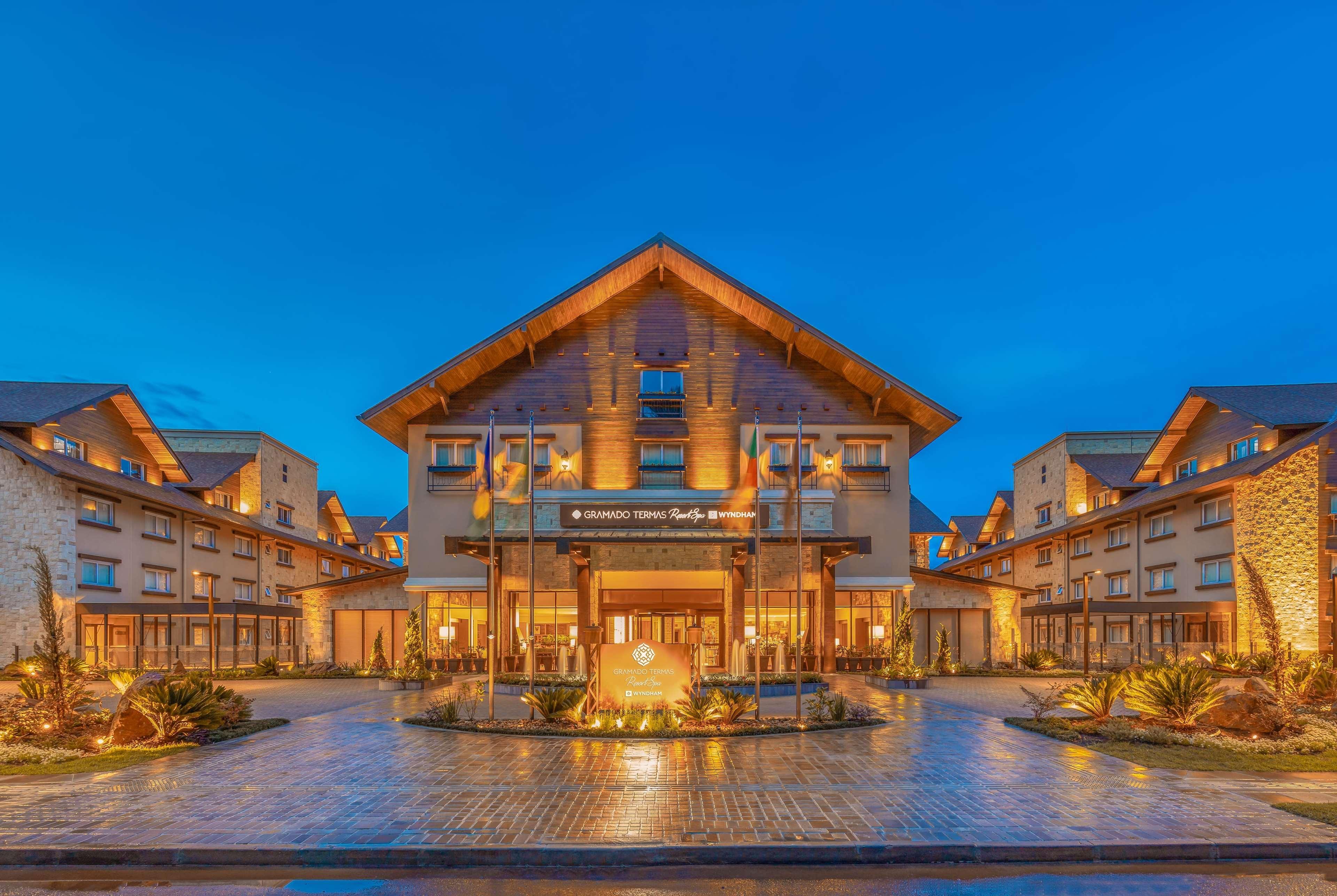 Wyndham Gramado Termas Resort & Spa Exterior foto The photo shows the exterior of a lodge or hotel. The building features a modern yet rustic design, characterized by wooden elements and a peaked roof. It is illuminated with warm lighting, creating an inviting atmosphere. The entrance is accentuated