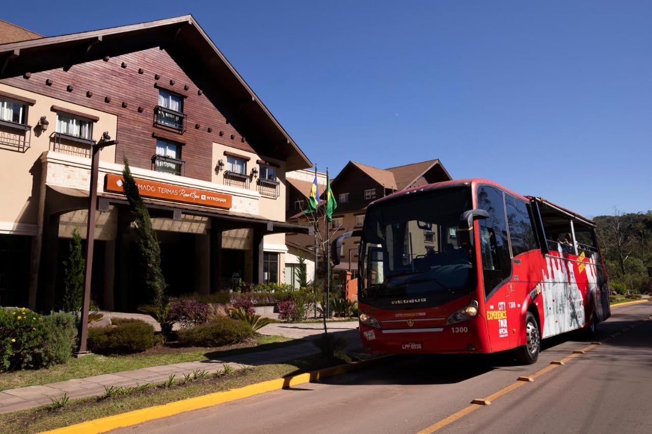 Wyndham Gramado Termas Resort & Spa Exterior foto The photo shows a red bus parked in front of a large building, which appears to be a hotel or lodge. The building features a rustic architectural style, with wooden elements and large windows. There are trees and landscaping around the entrance, and 