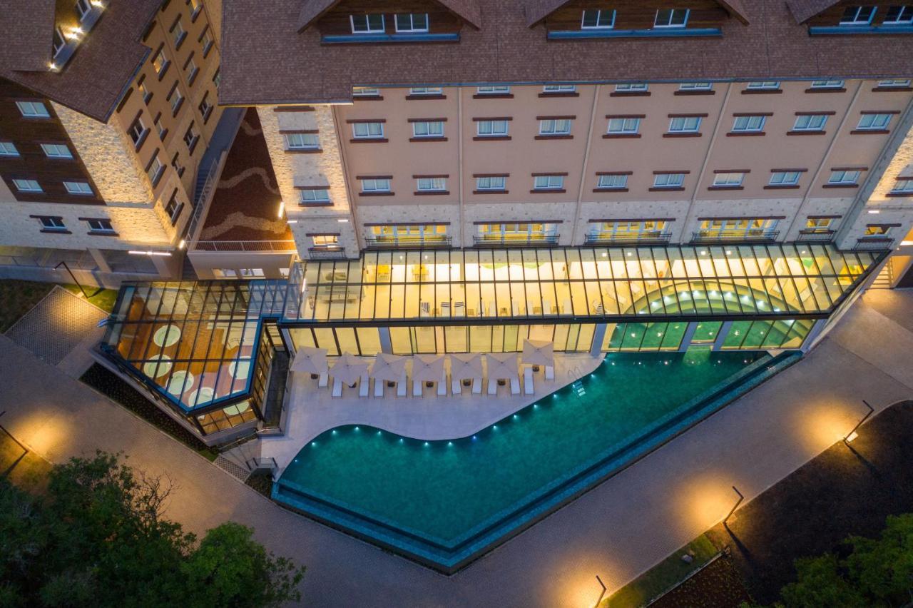 Wyndham Gramado Termas Resort & Spa Exterior foto The photo shows an aerial view of a hotel or resort complex. It features a building with a modern design and a combination of materials like stone and glass. Adjacent to the building is a rectangular swimming pool that has a unique shape, with lounge