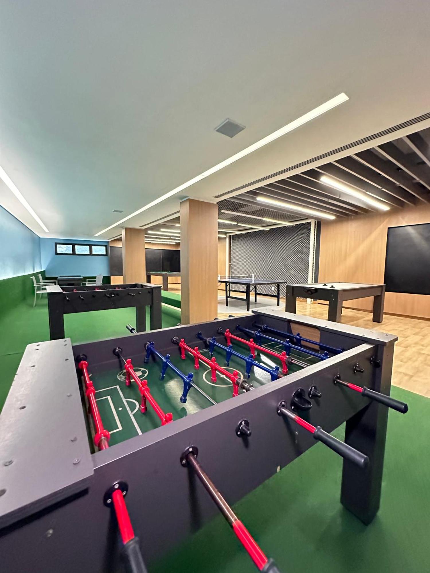 Wyndham Gramado Termas Resort & Spa Exterior foto The photo shows a spacious recreational area featuring several foosball tables. The tables are designed with red and blue players, and the floor has a green surface. The room is well-lit with modern lighting and has a contemporary design, including w