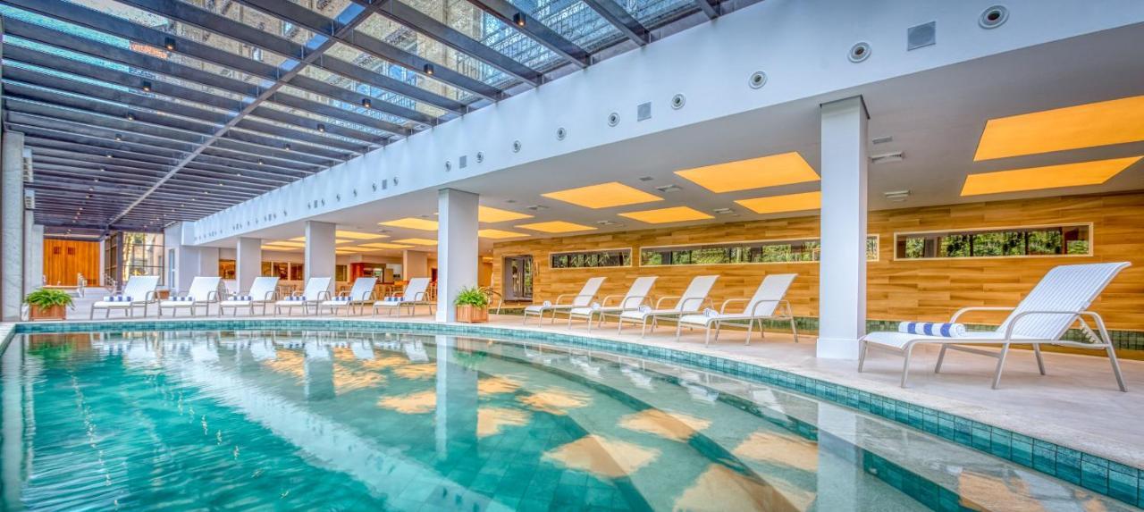 Wyndham Gramado Termas Resort & Spa Exterior foto The photo shows an indoor swimming pool area. The pool is surrounded by light-colored walls, and there are several white lounge chairs neatly arranged beside it. The ceiling features a modern design with beams and glass panels, allowing natural light