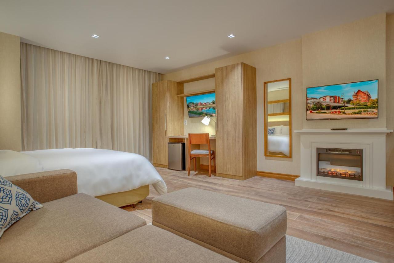 Wyndham Gramado Termas Resort & Spa Exterior foto The photo shows a modern hotel room that features a clean and minimalist design. There is a large bed with white bedding, and a sofa with cushions in a light color. The room includes a wooden entertainment unit with a flat-screen TV mounted above an 