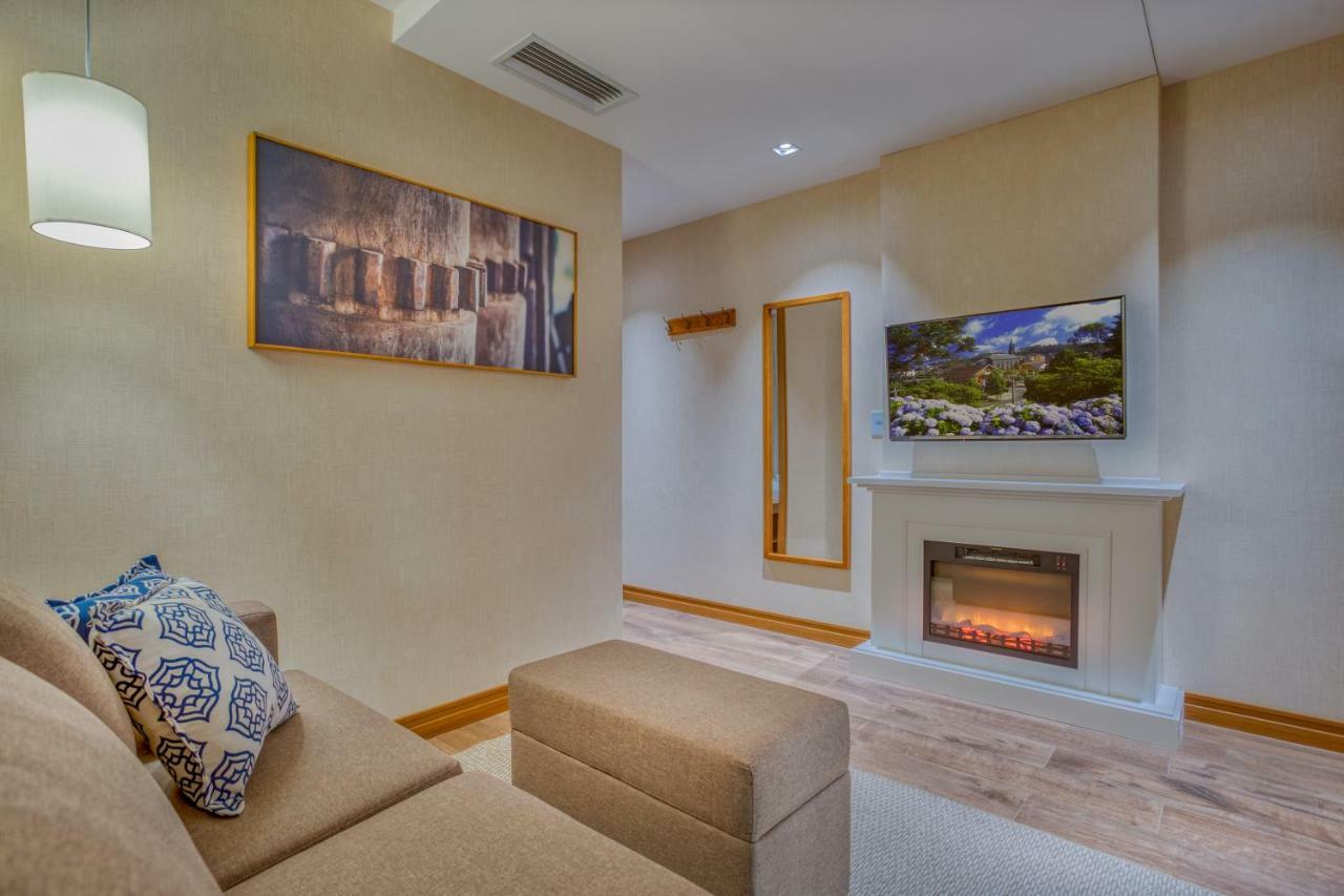 Wyndham Gramado Termas Resort & Spa Exterior foto The photo shows a cozy living room with a neutral color scheme. On the left, there is a light-colored sofa adorned with a decorative pillow featuring a geometric design. In front of the sofa, there is an ottoman. The opposite wall features a mounted 